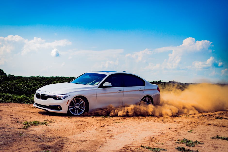 White luxury car drifting on a dirt road, creating a dramatic dust cloud under a blue sky